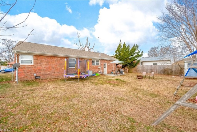 rear view of property with a fire pit, central air condition unit, a lawn, and a trampoline