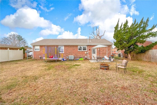 rear view of house with central air condition unit, a trampoline, a yard, and a fire pit