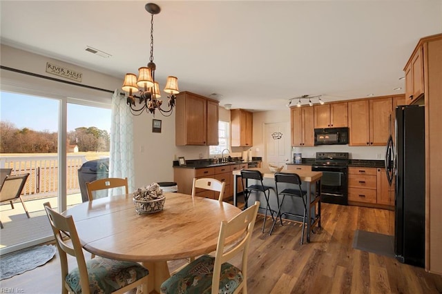 dining area featuring rail lighting, dark wood-type flooring, sink, and an inviting chandelier