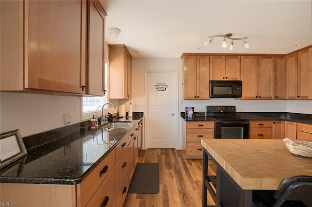 kitchen with sink, light hardwood / wood-style flooring, dark stone counters, and black appliances