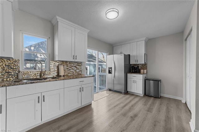 kitchen featuring sink, white cabinetry, dark stone countertops, stainless steel fridge, and light hardwood / wood-style floors