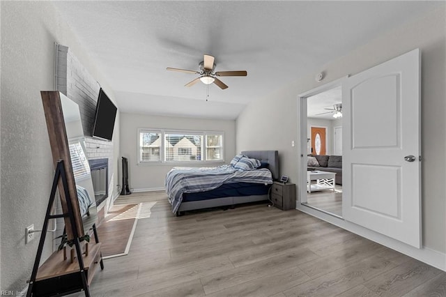 bedroom featuring ceiling fan, a fireplace, and light hardwood / wood-style floors