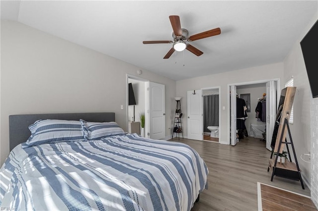 bedroom featuring vaulted ceiling, hardwood / wood-style flooring, a walk in closet, ceiling fan, and ensuite bath