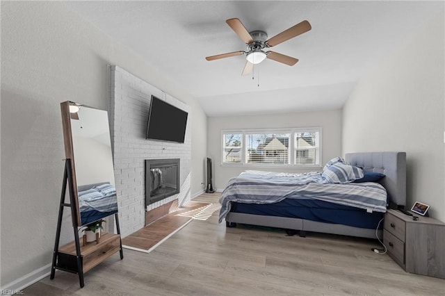 bedroom featuring ceiling fan, a fireplace, vaulted ceiling, and light wood-type flooring