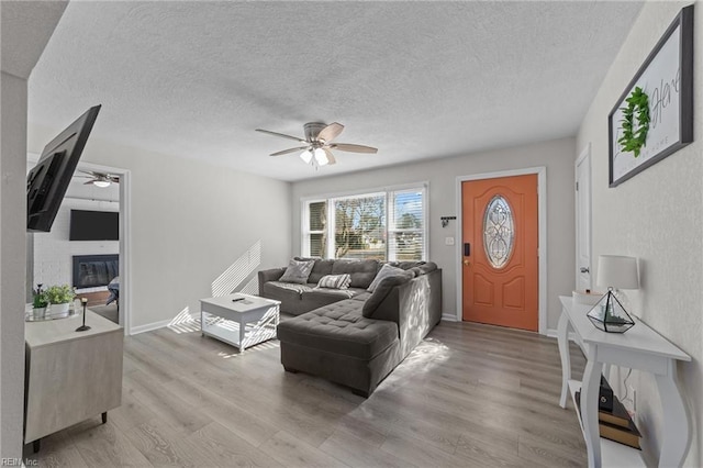 living room with ceiling fan, a textured ceiling, and light wood-type flooring