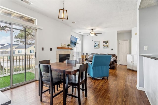 dining area featuring a tiled fireplace, dark hardwood / wood-style floors, and ceiling fan