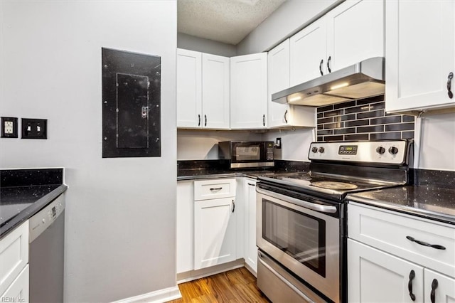 kitchen featuring white cabinetry, stainless steel appliances, dark stone countertops, electric panel, and light hardwood / wood-style flooring