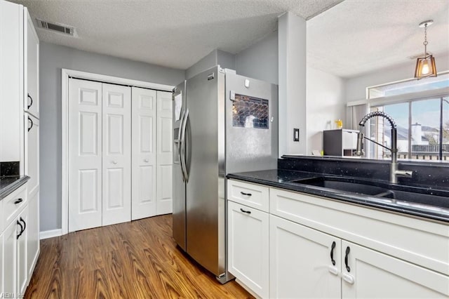 kitchen with a textured ceiling, wood-type flooring, sink, white cabinets, and stainless steel fridge