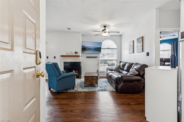 living room with ceiling fan, dark wood-type flooring, a textured ceiling, and a tiled fireplace