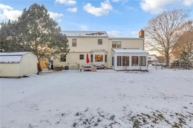 snow covered rear of property featuring a sunroom and a storage unit