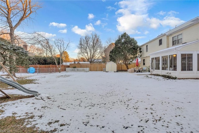 snowy yard featuring a shed and a sunroom