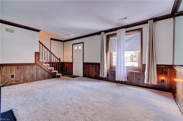 interior space featuring wood walls, a textured ceiling, light carpet, and ornamental molding