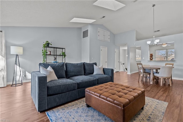 living room with an inviting chandelier, lofted ceiling with skylight, and light hardwood / wood-style floors