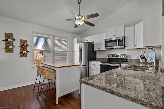 kitchen with lofted ceiling, sink, white cabinetry, appliances with stainless steel finishes, and a kitchen breakfast bar