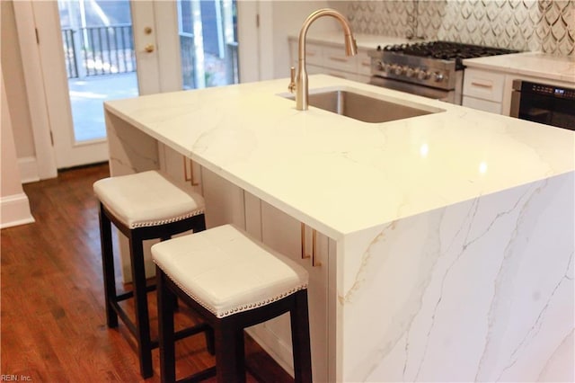 kitchen with sink, a breakfast bar, a kitchen island with sink, dark hardwood / wood-style floors, and high end stainless steel range