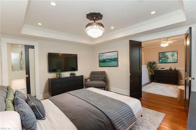 bedroom with ornamental molding, a notable chandelier, light wood-type flooring, and a tray ceiling