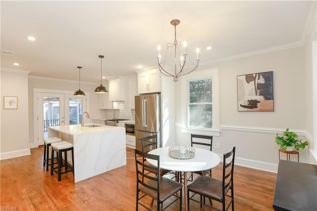 dining area with crown molding, sink, light wood-type flooring, and french doors