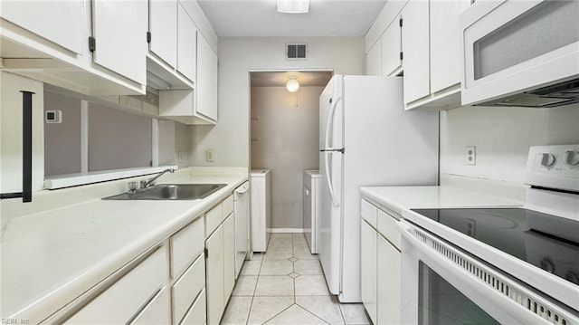 kitchen featuring light tile patterned flooring, white cabinetry, sink, white appliances, and washer and clothes dryer