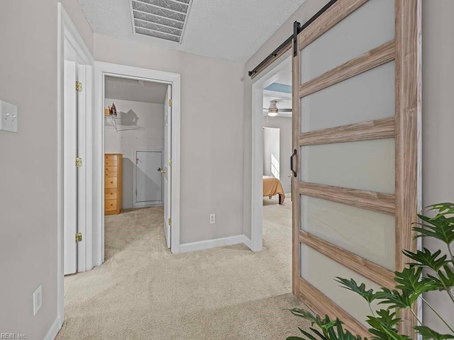 corridor with a textured ceiling, light carpet, and a barn door