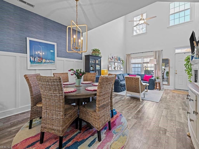 dining space featuring hardwood / wood-style flooring, a high ceiling, and ceiling fan with notable chandelier