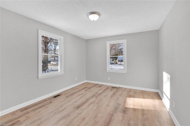 empty room with a textured ceiling and light hardwood / wood-style flooring