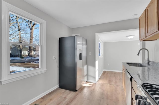 kitchen with sink, stainless steel appliances, light stone countertops, and light wood-type flooring