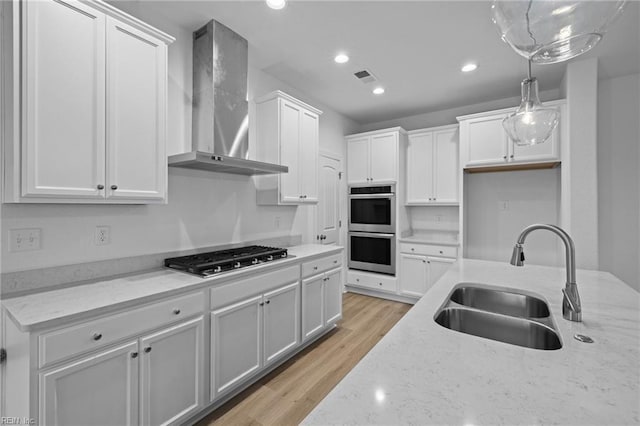 kitchen featuring sink, hanging light fixtures, wall chimney range hood, stainless steel appliances, and white cabinets