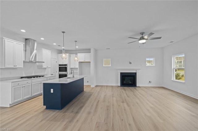 kitchen with white cabinetry, decorative light fixtures, an island with sink, and wall chimney exhaust hood