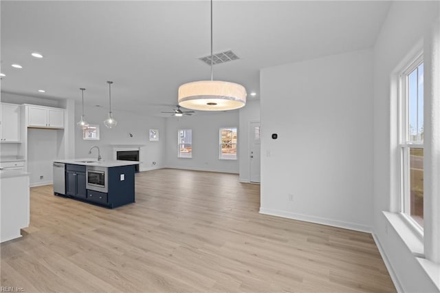 kitchen featuring pendant lighting, white cabinetry, stainless steel appliances, light hardwood / wood-style floors, and a center island with sink