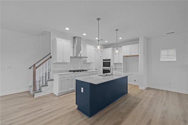 kitchen featuring white cabinetry, wall chimney range hood, and an island with sink