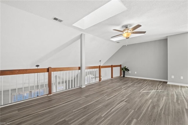 additional living space featuring hardwood / wood-style flooring, ceiling fan, lofted ceiling with skylight, and a textured ceiling