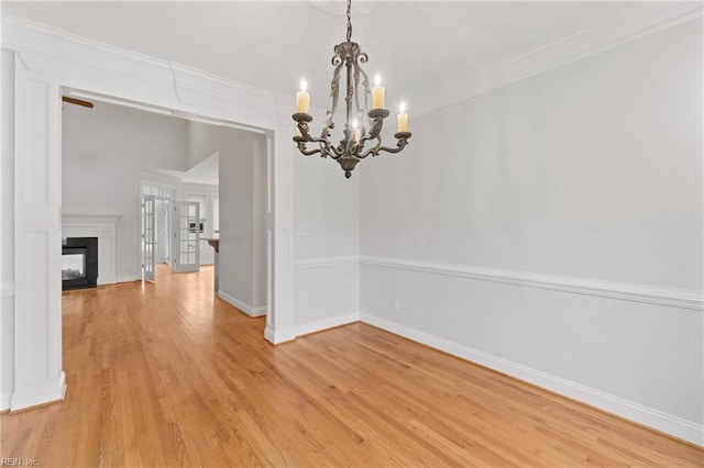 unfurnished dining area with a multi sided fireplace, wood-type flooring, ornamental molding, and a chandelier