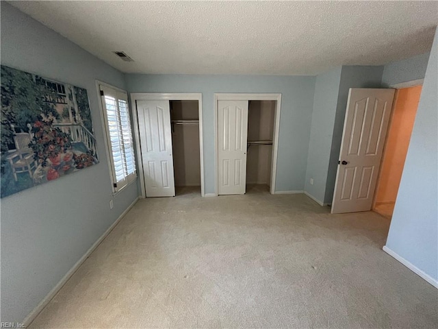 unfurnished bedroom with multiple closets, light colored carpet, and a textured ceiling