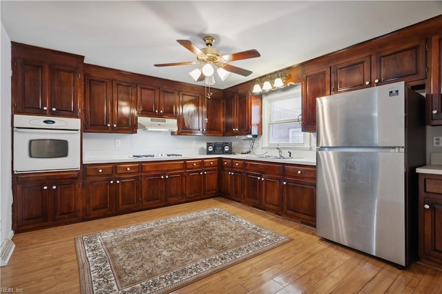 kitchen featuring tasteful backsplash, sink, ceiling fan, white appliances, and light hardwood / wood-style flooring