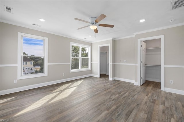 unfurnished bedroom with two closets, dark wood-type flooring, ornamental molding, and ceiling fan