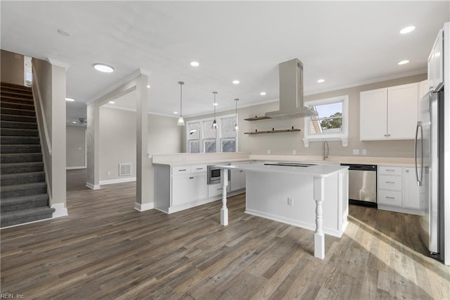 kitchen with appliances with stainless steel finishes, island range hood, white cabinets, and decorative light fixtures