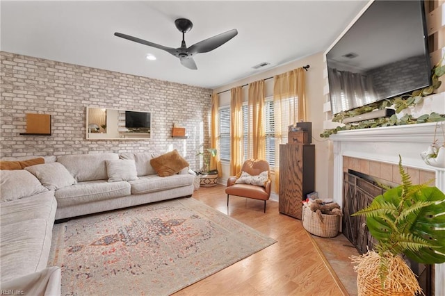 living room featuring light hardwood / wood-style floors, brick wall, ceiling fan, and a fireplace