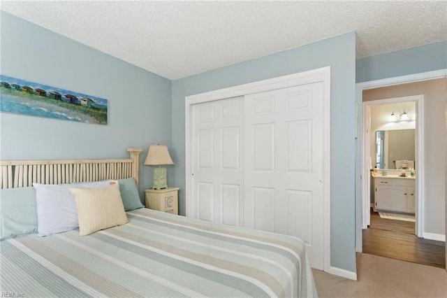 carpeted bedroom with ensuite bath, a textured ceiling, and a closet