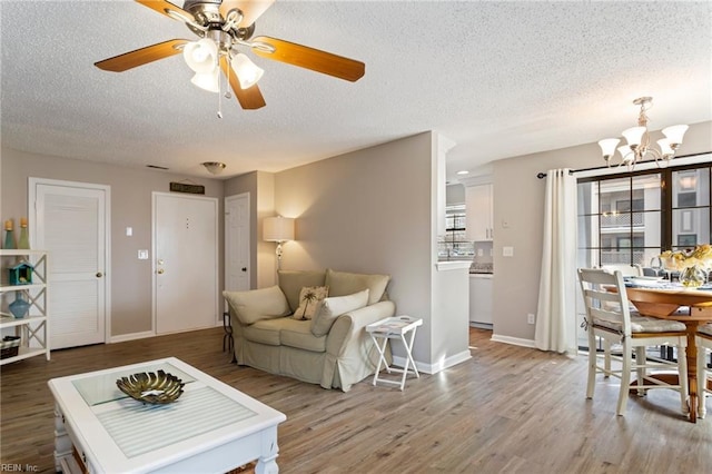 living room featuring hardwood / wood-style floors, ceiling fan with notable chandelier, and a textured ceiling