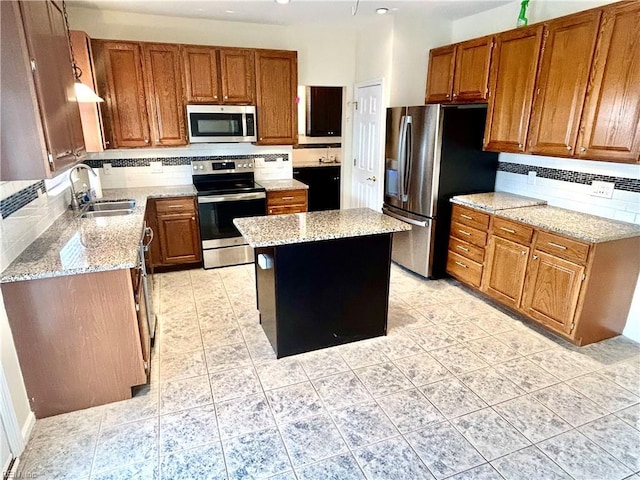 kitchen featuring appliances with stainless steel finishes, a center island, sink, backsplash, and light stone counters