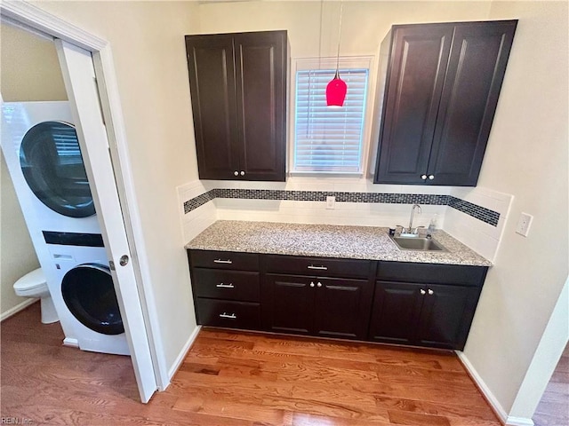 bathroom featuring sink, backsplash, toilet, stacked washing maching and dryer, and hardwood / wood-style flooring