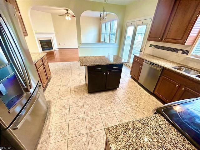 kitchen featuring a center island, hanging light fixtures, decorative backsplash, stainless steel appliances, and ceiling fan with notable chandelier