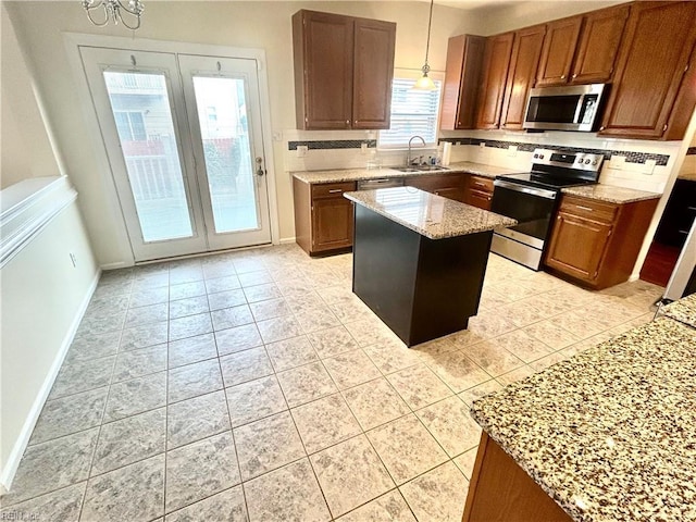 kitchen featuring hanging light fixtures, light tile patterned floors, light stone countertops, a center island, and stainless steel appliances