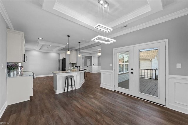 kitchen featuring decorative light fixtures, white cabinetry, stainless steel fridge, and a kitchen island with sink