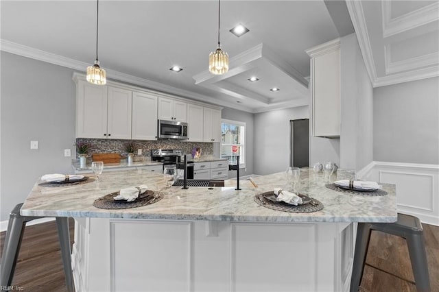 kitchen with decorative light fixtures, ornamental molding, a breakfast bar, and appliances with stainless steel finishes