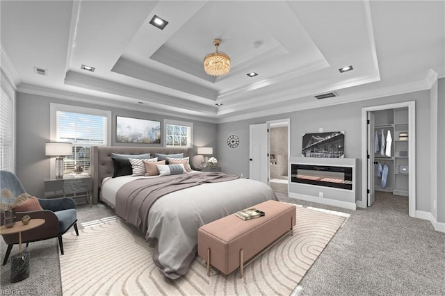 carpeted bedroom featuring a raised ceiling, ornamental molding, and ensuite bath