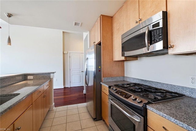 kitchen with appliances with stainless steel finishes, dark stone counters, hanging light fixtures, and light tile patterned floors