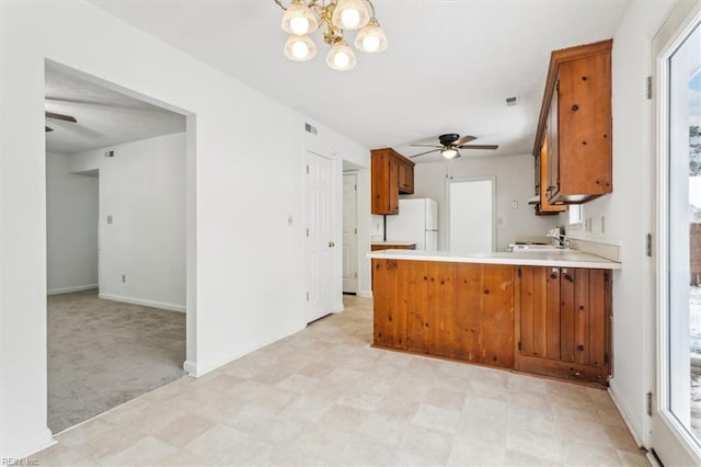 kitchen with sink, light carpet, kitchen peninsula, white fridge, and ceiling fan with notable chandelier