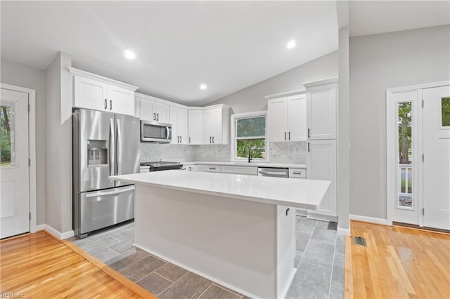 kitchen featuring white cabinetry, appliances with stainless steel finishes, a center island, and lofted ceiling