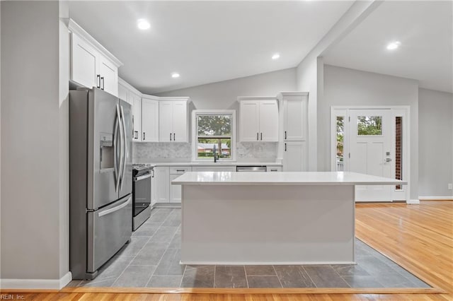 kitchen with white cabinets, a center island, vaulted ceiling, and stainless steel appliances